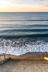 砂浜へ続く石階段と穏やかな波打ち際
