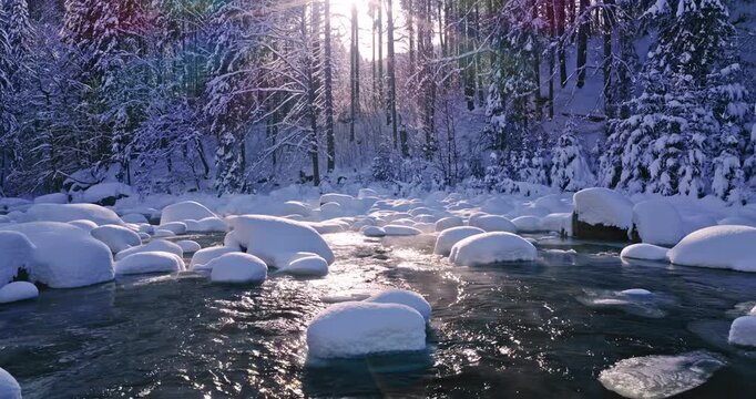Peaceful flight over a snow-covered alpine stream. Flowing icy water, frozen rocks, and fresh snow create a calm winter atmosphere ideal for relaxation, meditation, and nature visuals.