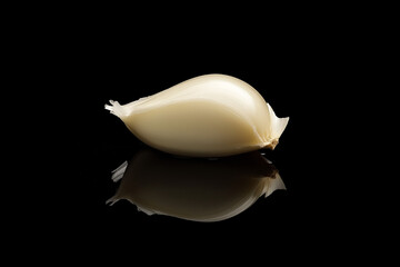 Fototapeta premium Minimal close-up of a single garlic clove isolated on a glossy black surface with subtle reflection, dramatic lighting, and high contrast emphasizing smooth texture and elegant simplicity