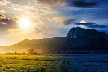 springtime in countryside. day and night time change concept. beautiful scenery with green grassy field with sun and moon. rocky cliff above the forested hill. duality and transition template