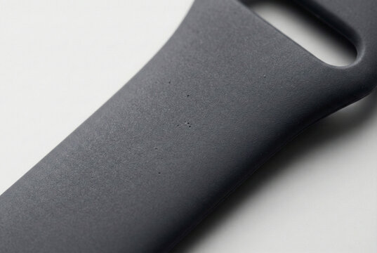 A macro close-up shot of a matte black silicone smartwatch strap, showcasing its fine micro-grain texture and subtle surface imperfections under soft, directional studio lighting.