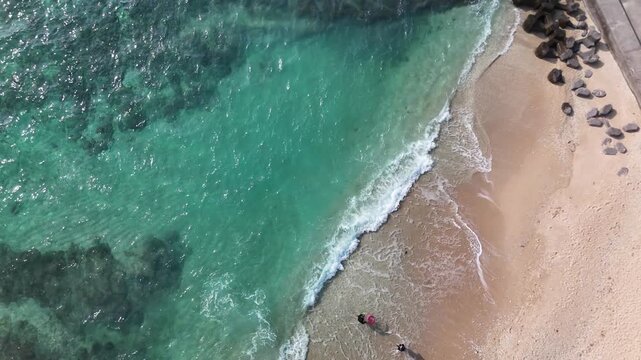 B roll aerial view of clear turquoise waters with waves crashing onto the beach creating dynamic motion natural patterns and a fresh coastal atmosphere