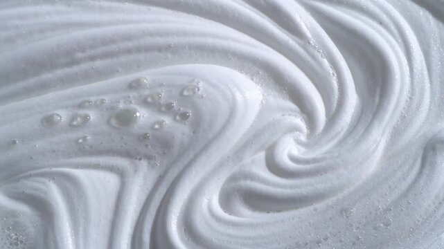 Thick white cosmetic foam swirling in smooth waves with small air bubbles representing soapy lather texture