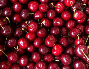 Full frame close-up of dark red cherries creating a dense fruit texture. Glossy cherry skins with stems and natural color variation, photographed from above for food textures