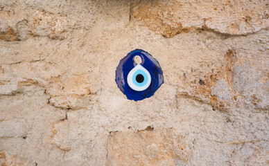A close-up of a blue nazar amulet affixed to a rough, textured stone wall. The vibrant blue eye contrasts with the earthy tones of the stone, symbolizing protection and cultural tradition.