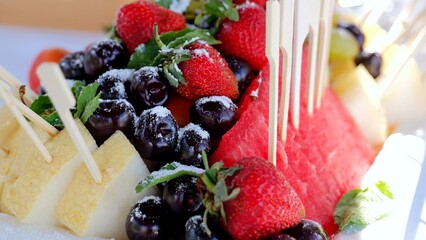 Fresh fruit assortment with watermelon, strawberries, cherries garnished by mint leaves, dusted...