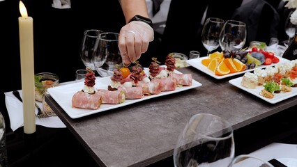 Professional chef wearing white gloves carefully positioning cherry tomato atop canape, completing gourmet appetizer platter for high end catered event