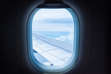 A view from an airplane window showing the aircraft wing and white clouds against a blue sky. Air travel, tourism, and journey concept.