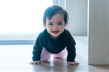 A happy Asian baby with a cheerful smile crawling on a wooden floor. Early childhood development, happiness, and healthy growth concept.