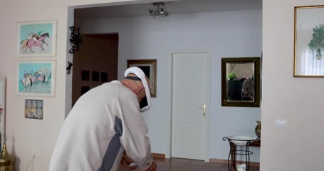 Senior man wearing a virtual reality headset and holding motion controllers while interacting with a virtual environment at home. Digital innovation, immersive technology, active aging. - Powered by Adobe