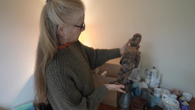 Mature woman explores family treasures and heirlooms while unpacking items from a box filled with memories and stories.