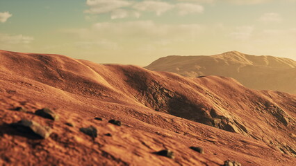 Naklejka premium Golden sunlight casts a warm glow on undulating hills in a tranquil desert. The landscape features scattered rocks, creating a peaceful atmosphere at dusk.