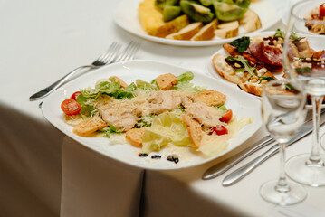 plate with caesar salad, cutlery and glasses on festive banquet table in restaurant