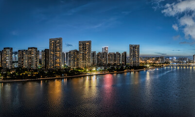 Stunning modern city skyline with illuminated skyscraper reflecting in the river at blue hour.