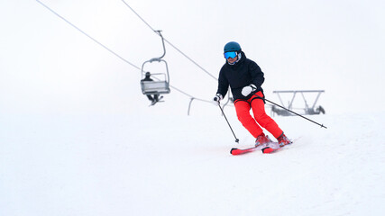 A skier moves along a white snowy slope at a ski resort, with a chairlift in the background. Snow flies out from under his skis.