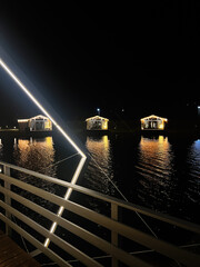Fototapeta premium Night lights on water: illuminated pavilions along a waterfront boardwalk at night with reflections