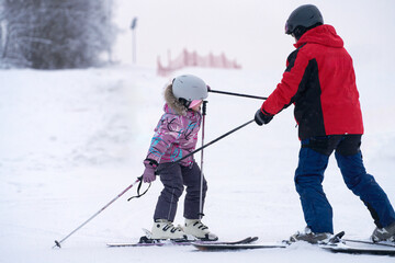 A children's instructor conducts a private lesson on a snowy slope to teach a child to ski.