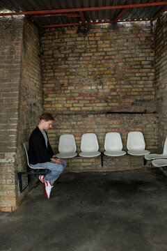Young man waiting alone in industrial interior with brick wall