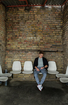 Young man waiting alone in industrial interior with brick wall