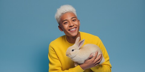 Happy young african male holding rabbit against blue background