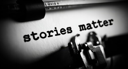 Close up vintage black and white image of the phrase stories matter typed crisply onto white paper inside an old fashioned mechanical typewriter machine