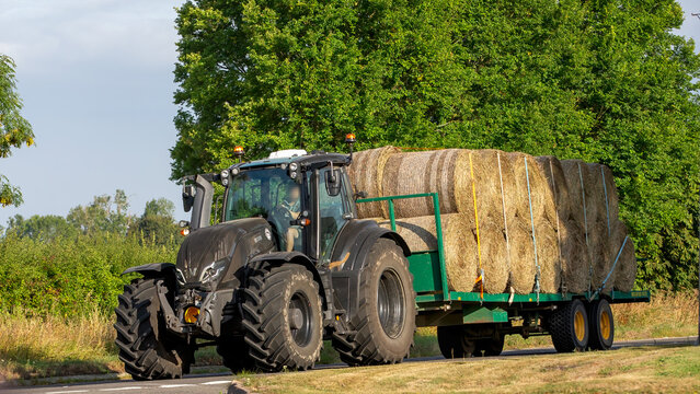 Whittlebury,Norhants,UK - Aug 23rd 2025:  Valtra tractor pulling a trailer loaded with straw bales  driving on a British road