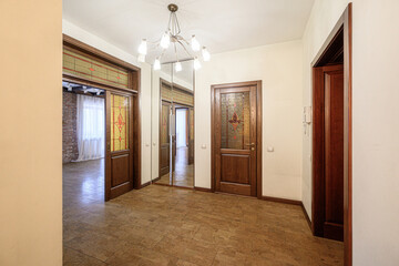 A spacious hallway with wooden doors featuring stained glass panels, a mirrored wardrobe, tiled floor, and a multi-arm chandelier. Warm and elegant interior.