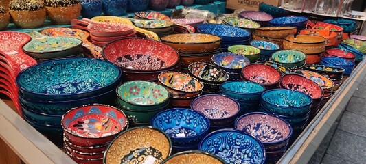 Assorted colorful handmade ceramic bowls and plates at a market stall, featuring vibrant glazed pottery and traditional artisan craftsmanship.