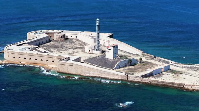 Aerial drone wide view of San Sebastian castle fortress and lighthouse in C&aacute;diz, Spain, Andalusia, Europe, on bright sunny day. Drone flying backwards. Cinematic grading