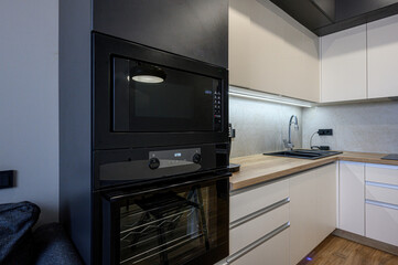 Obraz premium sleek modern kitchen with built-in black microwave and oven, white cabinetry, light wood countertops, black sink, stylish faucet, and under-cabinet lighting.