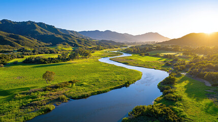 Fototapeta premium Serene landscape featuring winding river surrounded by lush green fields and mountains clear blue sky. warm sunlight creates peaceful atmosphere