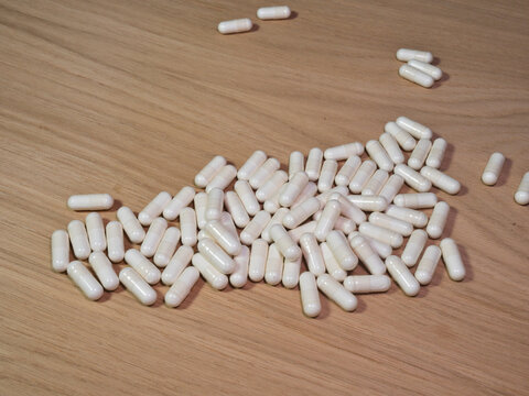 White medicinal capsules spilled on wooden tableA large cluster of generic white pharmaceutical capsules spilled haphazardly on a light brown wooden surface. Represents health, medicine, and overdos