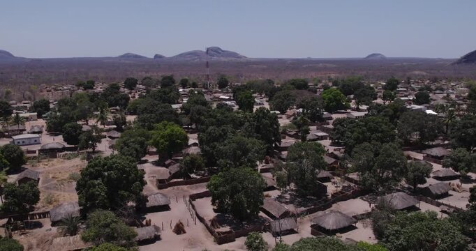 Aerial view of thatched roofs and lush green trees contrasting with the dry landscape, creating a textured scene, Lugenda, Niassa Province, Mozambique.