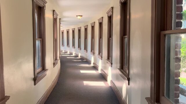 A long curved corridor features symmetrical windows, wood trim, and soft daylight. The interior architecture emphasizes repetition, perspective, and a quiet empty walkway.