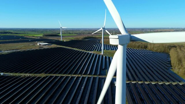 Aerial view of Chelveston Wind Farm with wind turbines and solar panels contrasting against the green fields under a clear blue sky, Wellingborough, United Kingdom.
