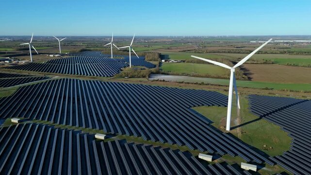 Aerial view of the Chelveston Wind Farm, where rows of solar panels meet wind turbines under a clear blue sky, Wellingborough, United Kingdom.