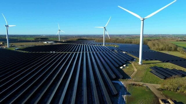 Aerial view of Chelveston Wind Farm showcasing solar panels contrasting with lush green fields and wind turbines against a clear blue sky, Chelveston, Wellingborough, United Kingdom.