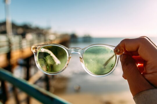 Hand holding clear sunglasses over a pier