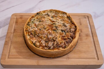 Delicious fresh homemade cooking spinach and feta quiche meal with shaved almonds on top. Perfectly baked tasty pastry crust oven food resting on wooden chopping board ready to serve