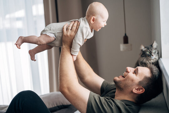 The middle plan of the portrait is in warm colors of a young father and newborn son. A father plays and kisses his little son on the bed. The concept of love, happy fatherhood.