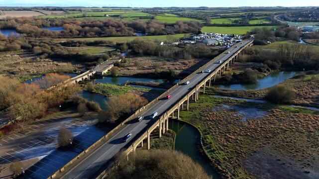 Aerial view of two bridges spanning waterways, cars traverse the newer bridge amid the golden hues of winter, Wellingborough, England, United Kingdom.
