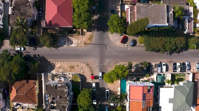 Aerial view of houses with red and green roofs, cars parked along the roads, and lush green trees, Maputo, Mozambique.