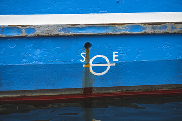Weathered blue ship hull with rust streaks and painted draft markings at waterline.
