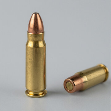 Close-up of a large-caliber cartridge with copper-jacketed bullet and polished brass casing on a light gray background