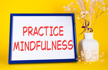 Mindfulness symbol. Concept words Practice Mindfulness on beautiful wooden picture frame. Beautiful yellow background with flower vase. Medical and Psychology concept. Copy space.