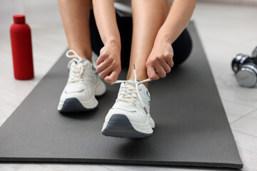 Woman in stylish sneakers training on mat indoors, closeup