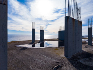 Obraz premium Construction site with concrete pillars near the shore under a bright sky with some clouds and a visible water reflection