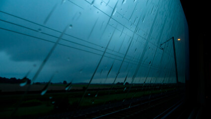 On the train car window the stormy dawn draws a wet diagonal: Rainy train window view with blurred landscape at twilight  