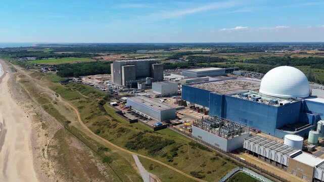 Aerial view of Sizewell C nuclear power plant contrasting with the beach and green fields under blue sky, Sizewell, England, United Kingdom.