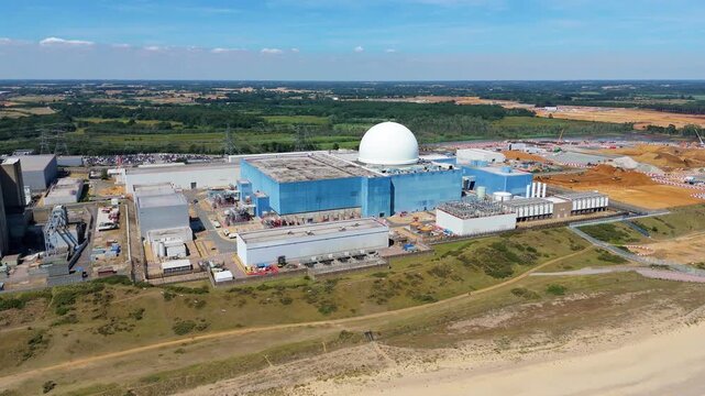 Aerial view of the Sizewell C nuclear power plant, where the blue buildings contrast with the surrounding green fields and brown earth, Sizewell C, England, United Kingdom.